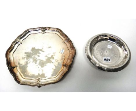An Eastern circular dish, with engine turned decoration, raised on three scrolled feet, possibly Turkish and a plated shaped 