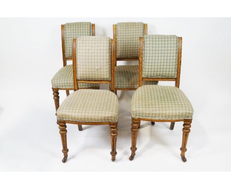 A set of four oak framed chairs by Maple and Co with upholstered backs and seats on turned tapering fluted legs with brass an