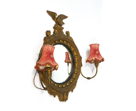 A regency style gilt convex mirror, the top crested with an eagle on a rocky crag. Between foliate scrolls. The glass surroun