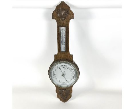 An oak aneroid barometer, with decorative flower head to the top, with silvered dial and blued steel indicator hand below a b