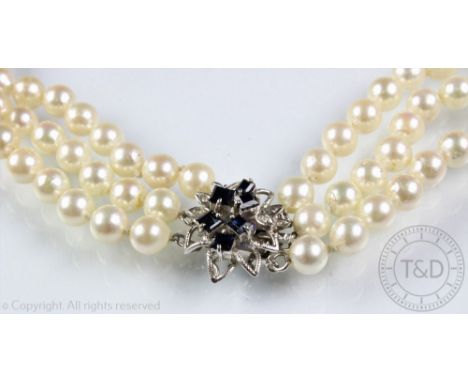 A three strand cultured pearl necklace with sapphire and diamond set white meatl foliate clasp stamped '14K 585', 34cm long o
