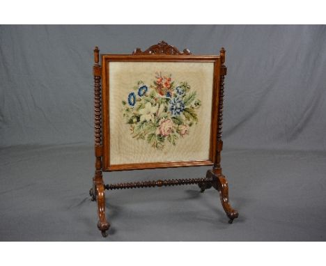 A VICTORIAN ROSEWOOD FIRESCREEN, carved top rail above a rectangular glazed panel containing a woolwork tapestry of a floral 