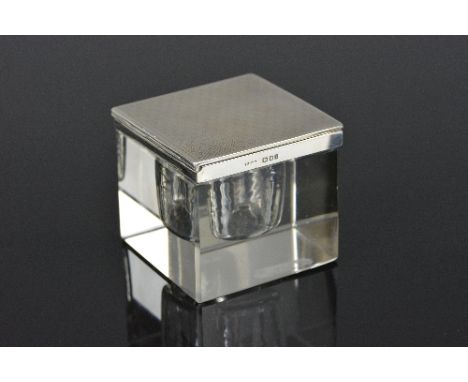 A GEORGE V SILVER AND GLASS INKWELL, of square form, the engine turned hinged cover above a glass base with silver mounted to