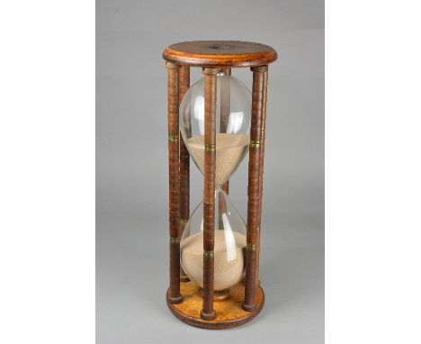 A LATE VICTORIAN/EDWARDIAN HOUR GLASS, circular turned treen end panels on six turned pillars enclosing a large sand filled g