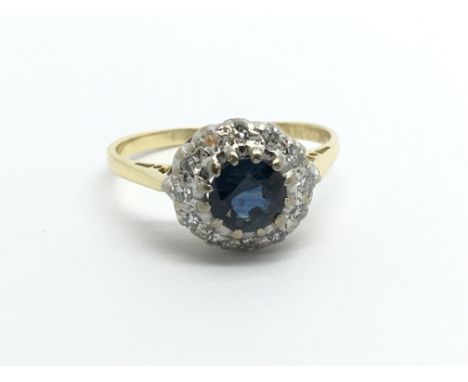 An unmarked yellow metal ring set with a central sapphire surrounded by diamonds, approx 2.4g and approx size I.