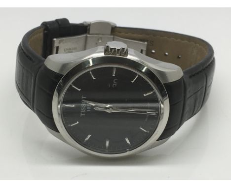 A gents Tissot watch with a black face and silvered baton numerals on a black leather strap.
