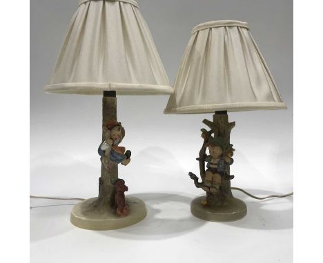 A pair of Goebel-Hummel pottery table lamps, circa 1930, modelled as children seated on the branches of a tree, 26cm high (in