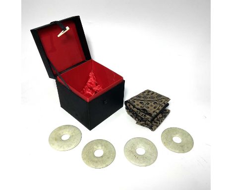 A set of four Chinese green jade type ring discs, together with fabric napkins, in satin covered box, 7.5cm diameter (4)