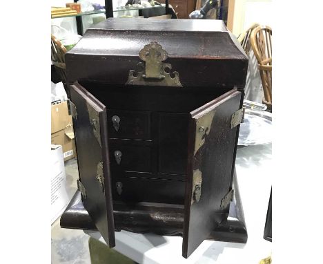 A Chinese table top cabinet, fitted cushioned lift up lid above two doors revealing trinket drawers, on cushioned base with c