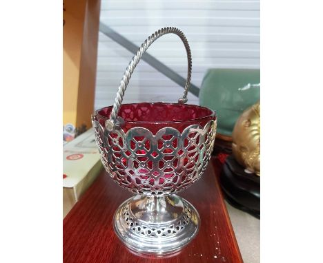 An electroplated bon bon basket with ruby glass liner, together with two plated candlesticks on ogee stepped bases (3)