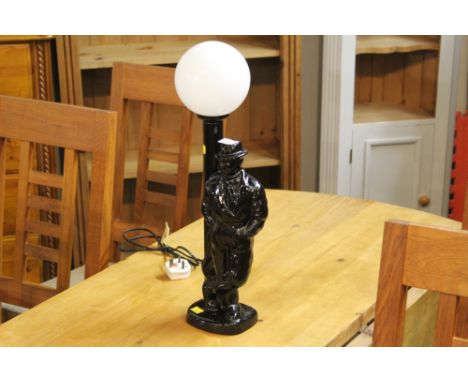 Modern black glazed ceramic table lamp, in the form of a figure leaning against a lamp post, with spherical opaque glass shad