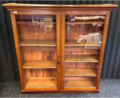 A contemporary bookshelf, the moulded cornice over two glazed cupboard doors opening to shelved interior [134.5x136x35.5cm]