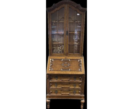 An oak Bureau book case, the shaped cornice over two glazed panel doors opening to shelved interior the lower with slope abov