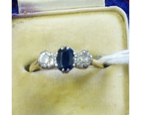 An 18ct gold sapphire and diamond three stone ring claw set with an oval mixed cut stone, flanked by old cut diamonds