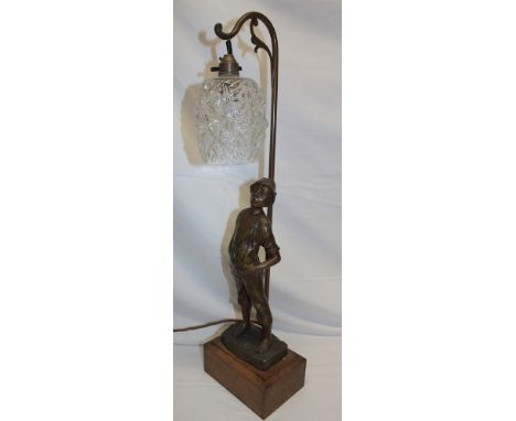 A bronzed spelter table lamp in the form of a young boy beneath a scroll lantern with glass shade on a rectangular wooden bas