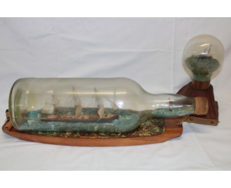 A good quality wooden scale model ship in a bottle 20" long overall and one other glass sphere containing a model boat (2)