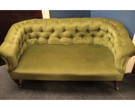 A Victorian mahogany three-seat Chesterfield sofa upholstered in green buttoned fabric on turned legs with castors