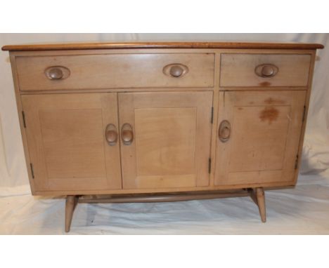 A 1960's Ercol pale elm sideboard with two-drawers in the frieze and cupboard enclosed by three panelled doors on tapered leg