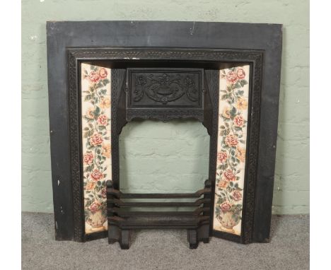A cast iron fireplace and grate, featuring tiled sides with flowers. Bearing stamp for 'Fireplace World' to reverse.  