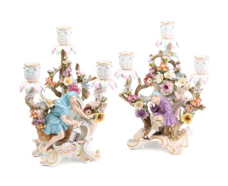 A pair of Meissen three branch candelabra, depicting a figure seated with a spilling bag of gold and Diogenes holding a lante