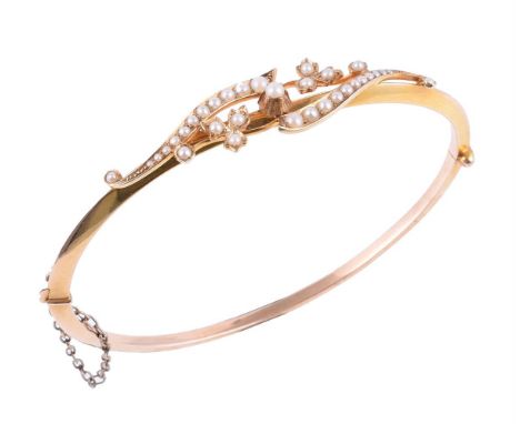 An Edwardian half pearl hinged bangle, circa 1910, the gold foliate crossover panel set with graduated half pearls, stamped 1