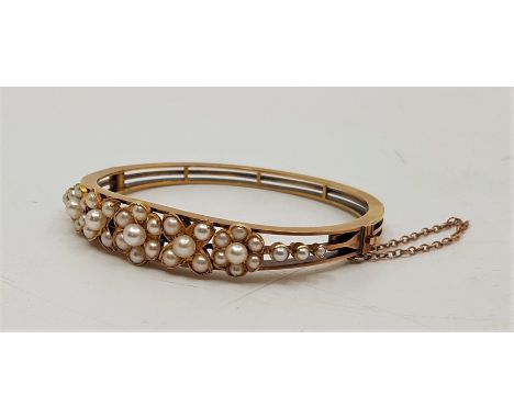An antique precious yellow metal and cultured pearl set floral hinged bangle, the front having applied flower form mounts set