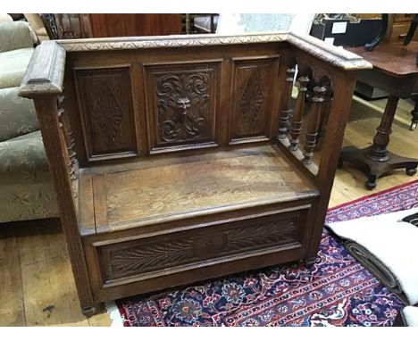 An Edwardian carved oak settle, the panel back enclosed by turned pilasters, above a hinged seat, raised on tapering feet (h.