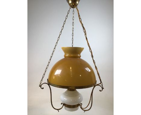 A hanging oil lamp with glass shade and reservoir with brass chains and decorative brass brackets that has been converted to 