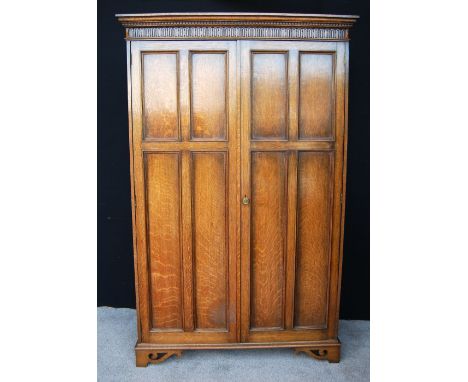 Oak two-door wardrobe by Waring & Gillows, the projected moulded cornice over fluted frieze, panelled doors enclosing mirror,