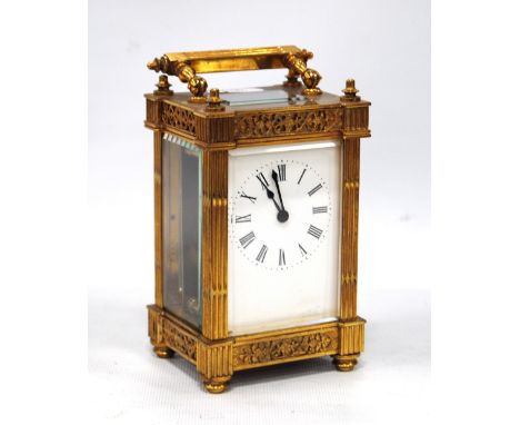 Brass carriage clock mounted by a fluted handle, chased fretwork to the frieze, white enamelled face, Roman numerals and rais
