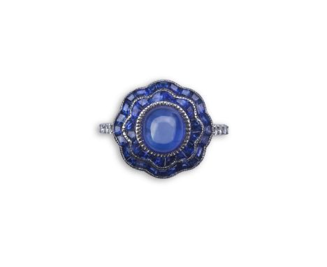 A sapphire ring, of Art Deco inspiration, set with a cabochon sapphire within a floral double border of calibré-cut sapphires