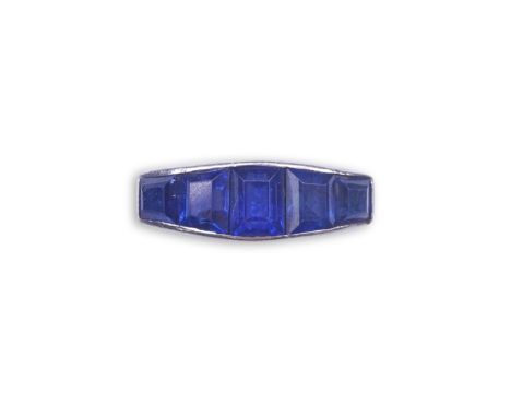 An Art Deco sapphire ring, 1930s, designed as a sequence of five channel-set calibré-cut sapphires, to a scrolled gallery and