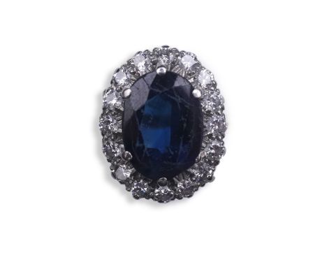 A sapphire and diamond ring, of cluster design, claw-set with an oval deep blue/green sapphire weighing approximately 2.50 ca