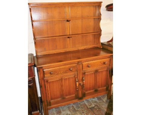 An Ercol elm dresser, with a two shelf waterfall plate rack, over a pair of doors above cupboard doors with sliding latch, ra