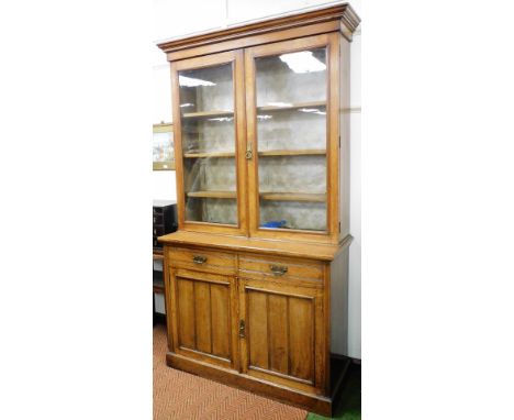 A Victorian oak cupboard bookcase, the out swept pediment over a pair of glazed doors enclosing three shelves, above two draw