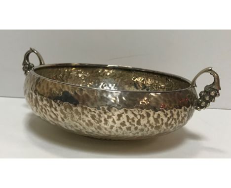 A hammered silver two-handled bowl, raised on a beaded circular foot and flanked by grape and vine handles, initialled to bas