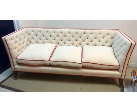 A Lawson Wood cream buttoned knowle style three seat sofa with scarlet velvet piping, raised on square tapered legs to castor