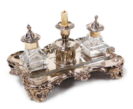 A Victorian silver plated desk stand, of serpentine form, with a gadrooned and floral embossed border, raised on four scroll 