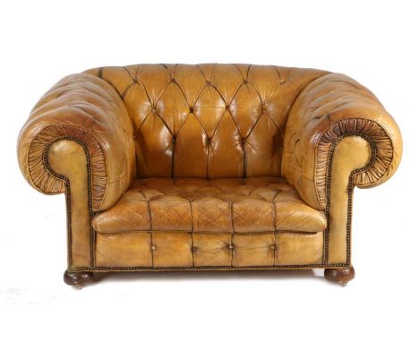 A leather upholstered deep armchair, the button back and scroll arms above the button seat raised on bun feet, 134cm wide, 98