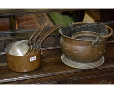 A set of five graduated copper pans; a helmet shaped copper coal scuttle; a brass planter. (7)