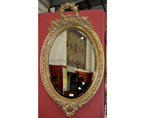 A gilt framed oval wall mirror, the frame decorated with sheaths and flora.