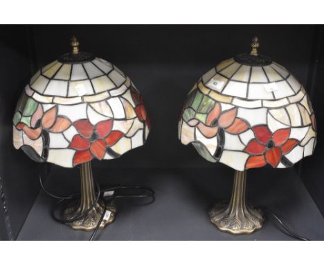 A pair of modern attractive Tiffany style electric table lamps, with decorative leaded glass shades and spreading trunk form 