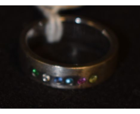 An 18ct white gold multi stone brushed matt effect band ring. inset with a row of six different coloured stones, stamped 18k,