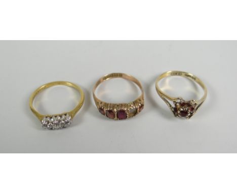 Three gold rings including three-stone diamond ring, garnet ring (one stone missing) Condition Report: please request via ema