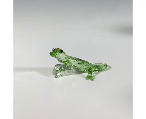 A small, green, multi-faceted reptile with smooth features, adorned with black eyes and red gemstones on its head, perched at