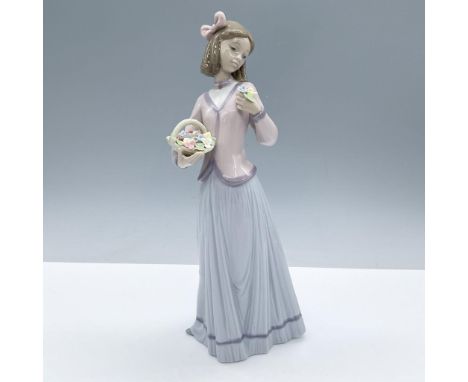 Glossy figurine of a girl gazing at the flowers in one hand while holding a basket of them in the other. Depicted in soothing