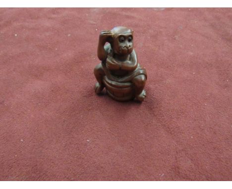 An Oriental carved wood netsuke of a monkey washing 
