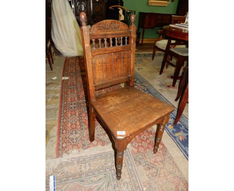 An Oak framed solid seated Hall Chair having turned and fluted front legs, the back rest with bobbin turned details, carving 