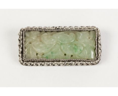 CHINESE SILVER COLOURED METAL OBLONG BROOCH, framing a foliate carved and pierced pale green jade oblong panel, 2" wide, 1" h