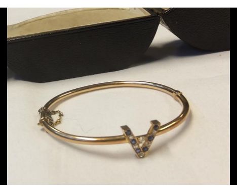 A ladies elegant yellow metal bangle with diamond and sapphire mount in the form of the letter 'A' - in presentation case
